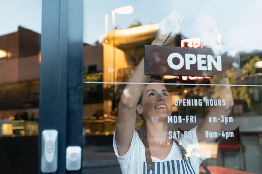 Woman switching sign at the front of her store to OPEN