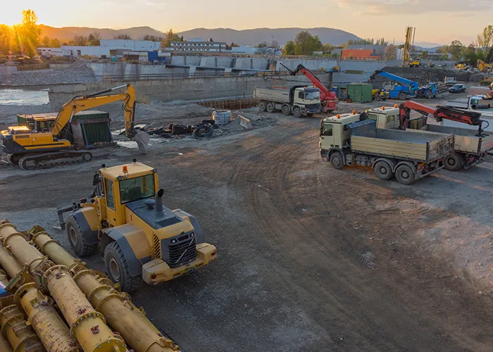 Heavy equipment and job trailers on a construction site at dusk.