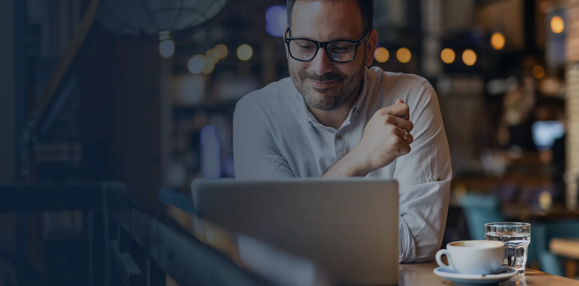 Man sitting at a table in a restaurant working on a laptop computer.