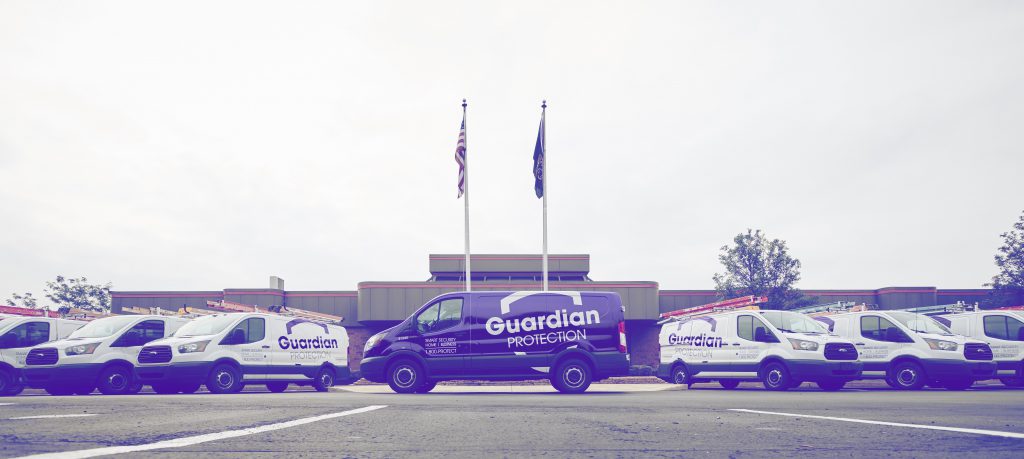 White Guardian Protection vans with purple logos lined up on either side of a purple Guardian van with a white logo. 