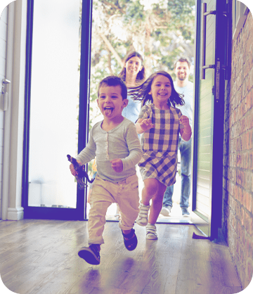 Two young children excitedly running into the house in front of their parents