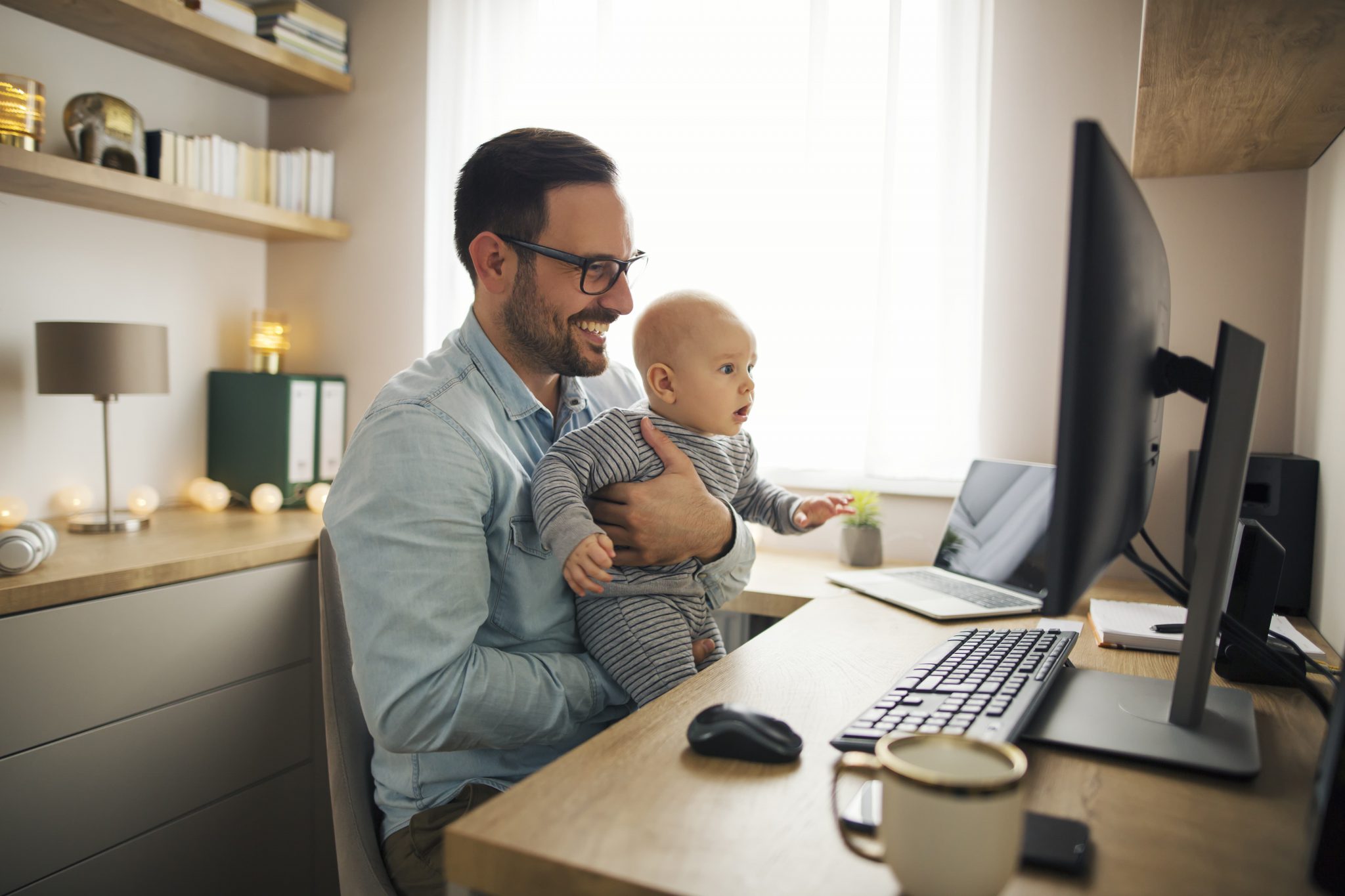 Father looks at computer with baby in lap