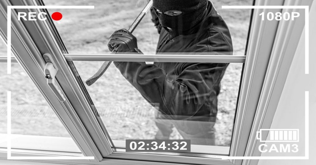 Masked burglar using crowbar to open glass sliding door