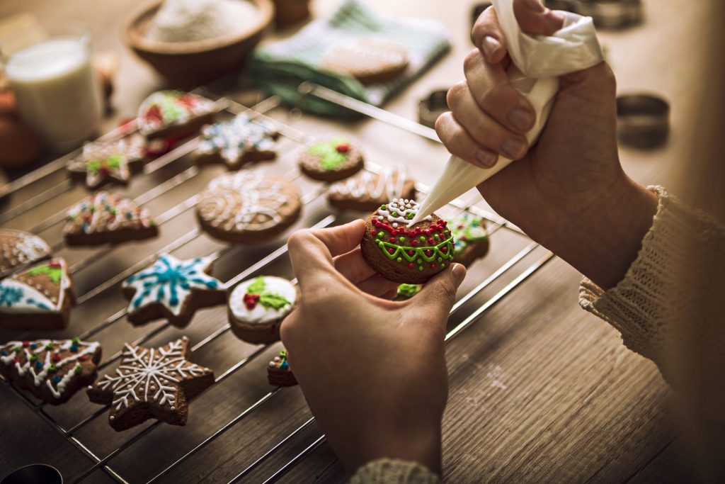 Holiday cookies cooling on rack with baker decorating one with icing