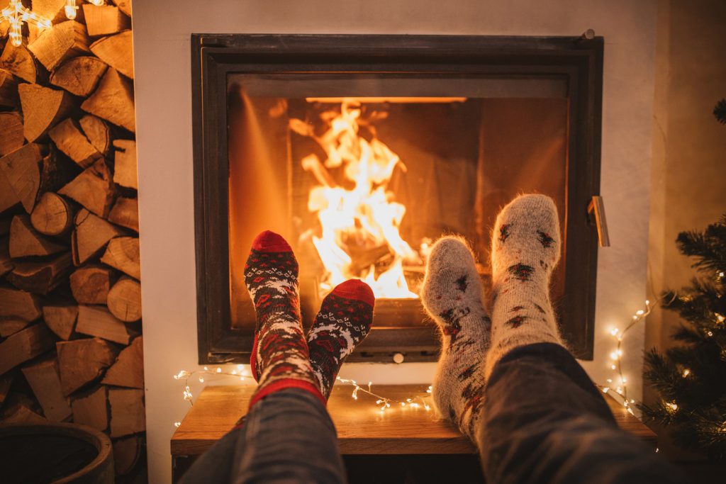 Two pairs of feet wearing holiday socks propped up in front of a fireplace with fire burning