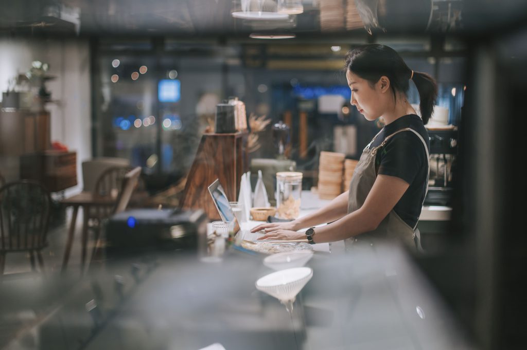 Female owner working at restaurant counter on her laptop.