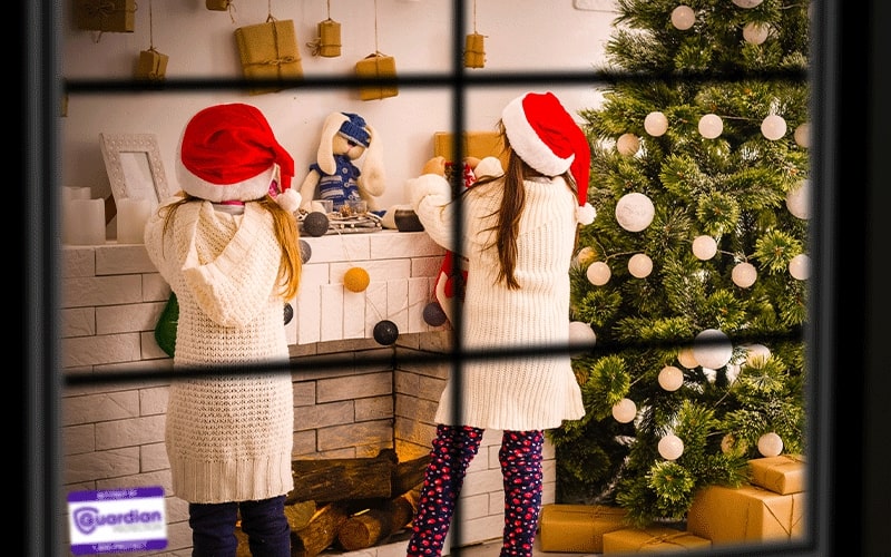 Two girls wearing Santa hats hanging stockings on a fireplace