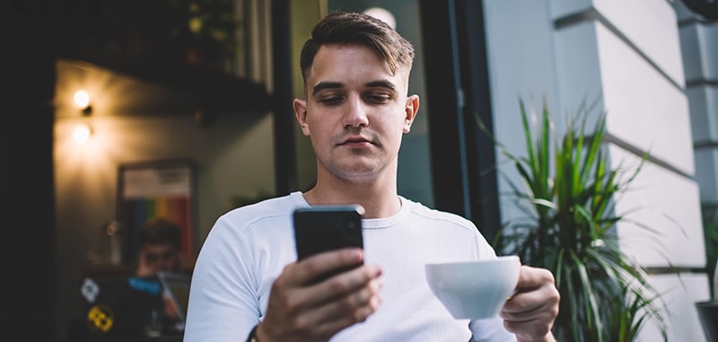 Man drinking coffee and checking Guardian Protection app notifications on smart phone