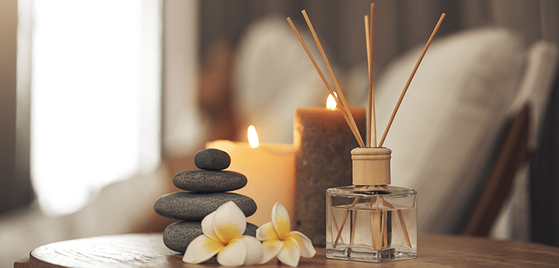 Two burning candles and room diffuser set on top of a living room end table