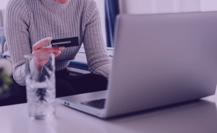 A person sitting at a laptop with their credit card out, about to make a purchase