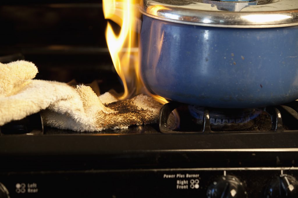 A kitchen towel catching fire from the flame of a stove top burner.