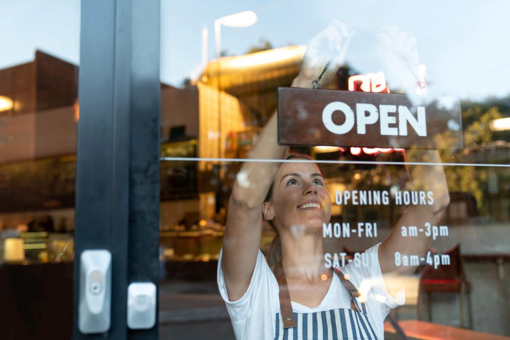 Woman switching sign at the front of her store to OPEN