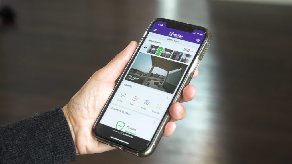 Hand holding iPhone open to Guardian Protection app with outdoor camera view of front yard