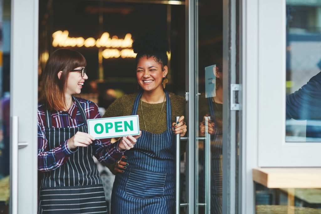 Two small business owners holding up an open sign