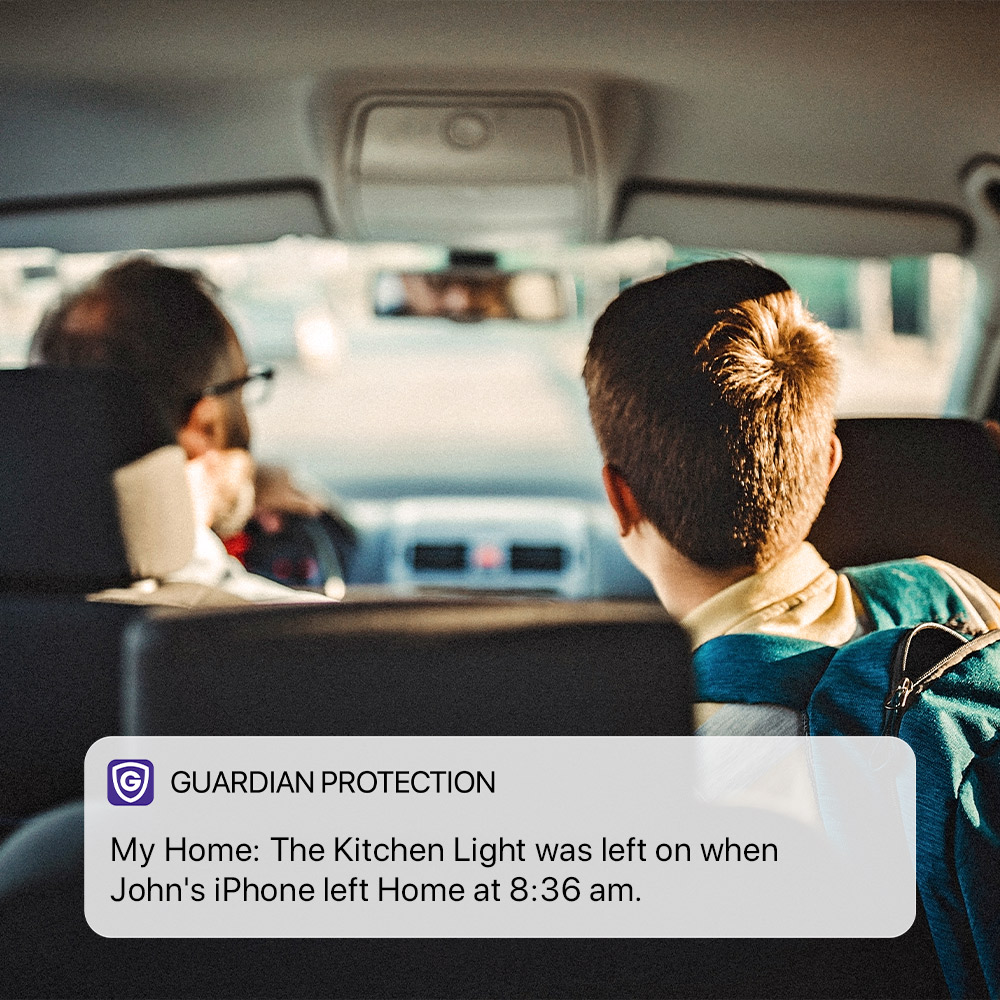 Father and son driving in a car with Guardian mobile app notification showing smart light reminder.