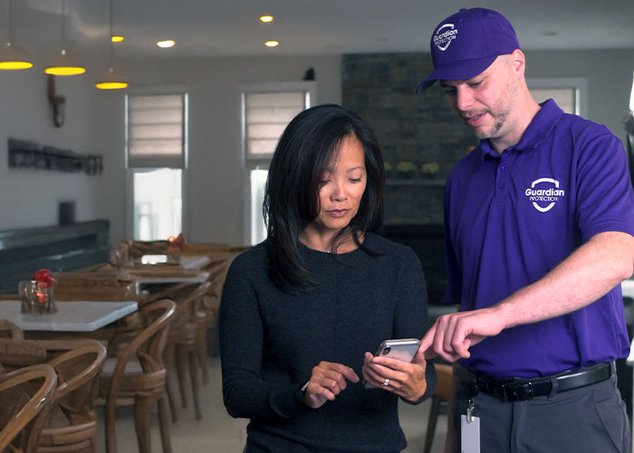 Guardian Protection technician helping a restaurant manager set up her smart business security from her phone.