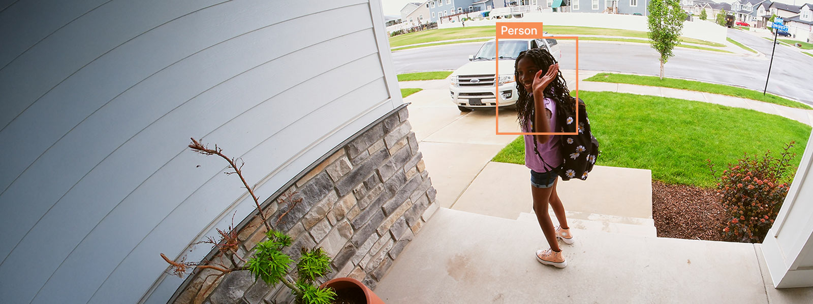 Young girl waving to a video doorbell camera from her home's porch