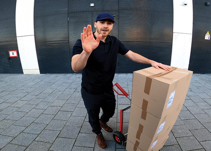 View of delivery man with packages waving at camera to receive access via Guardian's video concierge service